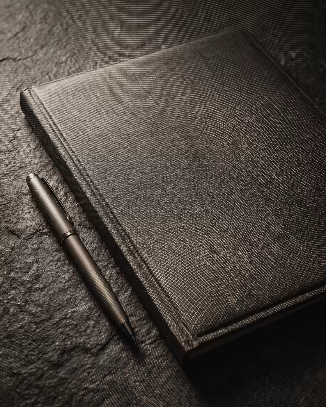 Una carpeta encuadernada en lino, cerrada, sobre una mesa de piedra junto a una pluma