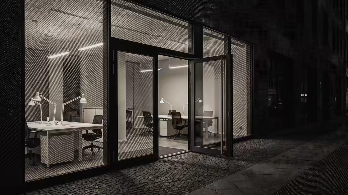 Una oficina a pie de calle al amanecer, con las luces encendidas y la puerta de vidrio abierta