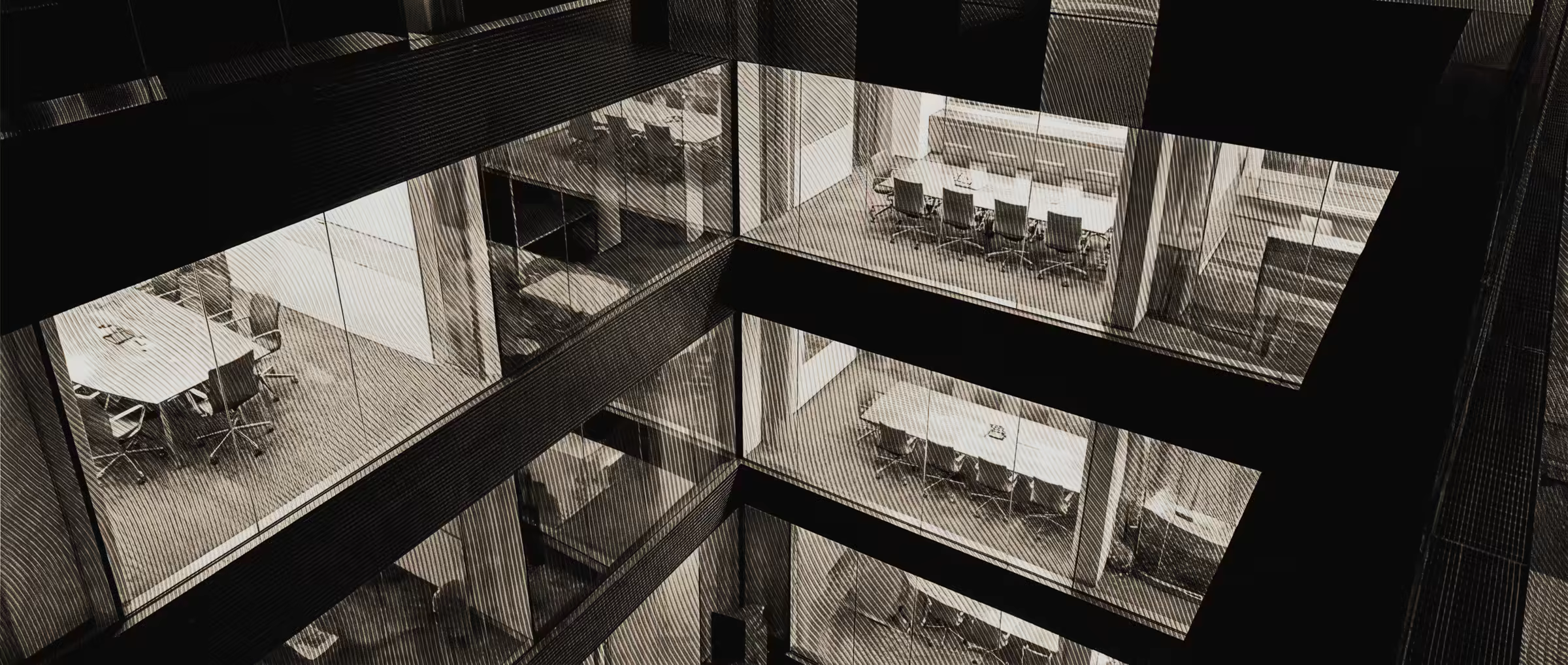 Un atrio de oficinas de noche, visto desde arriba, con las salas de reuniones iluminadas y vacías
